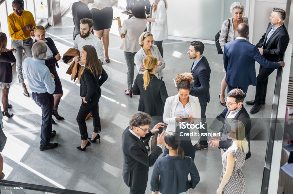 A diverse group of male and female business professionals actively networking at a conference. Attendees in formal attire discuss ideas and opportunities in a modern venue, highlighting collaboration and innovation in the corporate world.