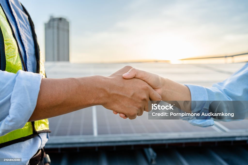 Two Electrical Engineers shaking hands after working to inspect the installation and maintenance of solar panels in the solar power station, Renewable Energy, sustainable business concept.